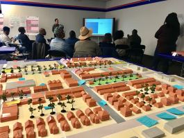 Residents and other stakeholders hear the results of the three-day design charrette to reimagine Whitehaven Plaza. In the foreground, the model of Whitehaven Plaza shows existing structures in gray alongside new buildings, greenspaces and amenities s