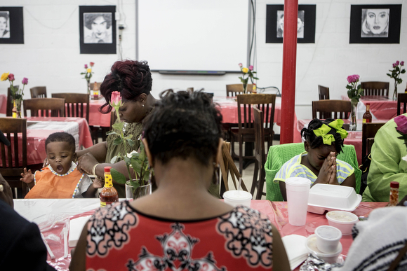 Ashley Barnes (second from left) says grace with her family while putting a bib on her son Ayden, 1.