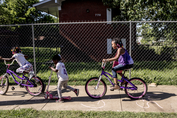 Girls ride their bikes down Tate Avenue past a boarded up apartment complex.