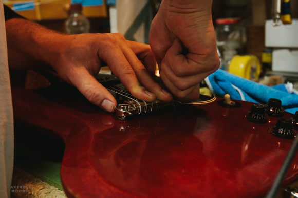 Hans Hilboldt tightens down the strings recently installed on an electric guitar.