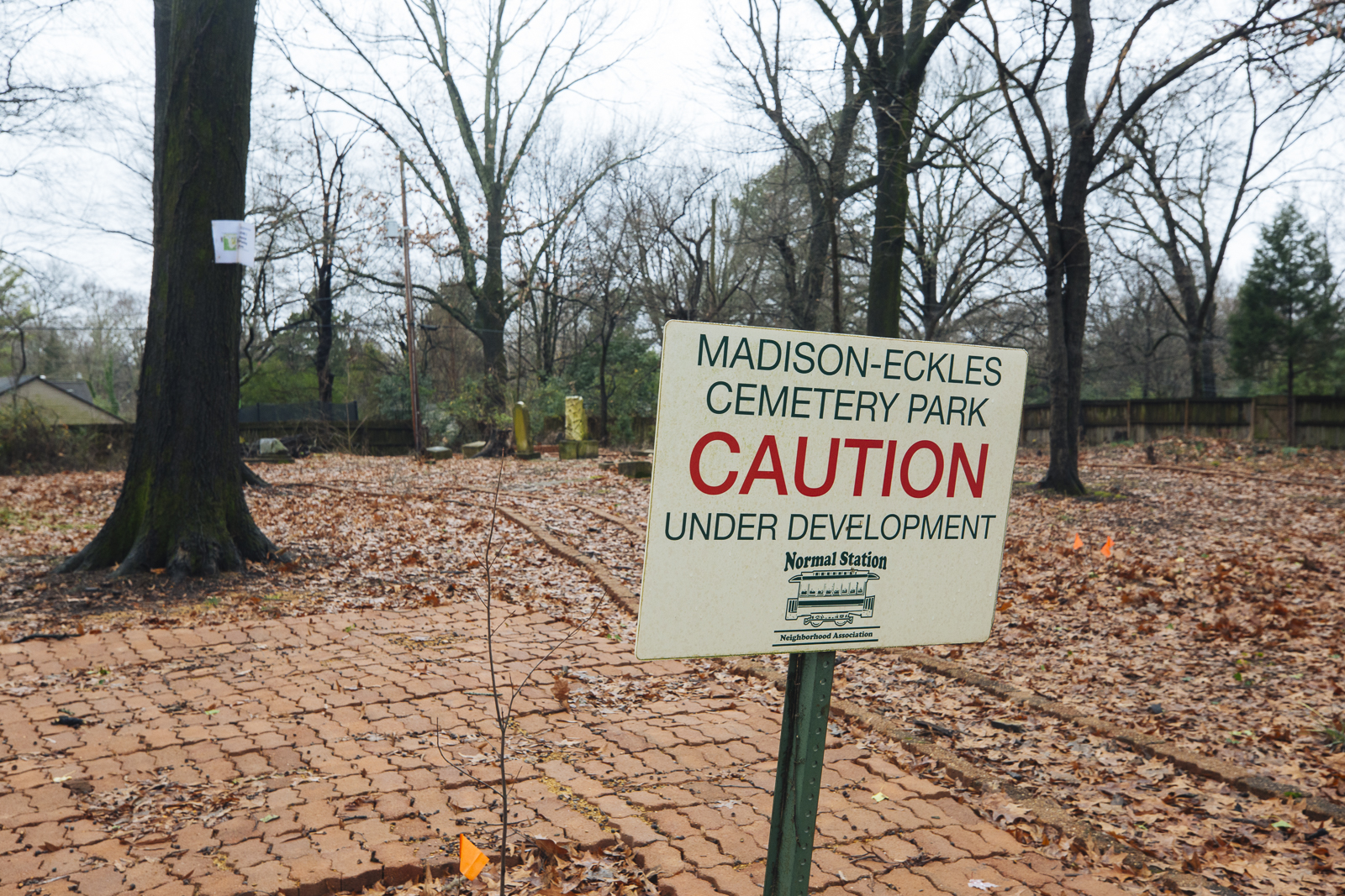 A sign at the entrance of Madison-Eckles Cemetery Park cautions visitors that the park is still under development. A brick lined path to the right of the patio area leads to the cemetery, located in the center of the park. (Ziggy Mack)
