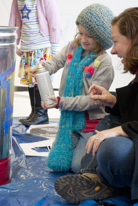 Volunteer Chandler Pritchett shares her enthusiasm with her daughter, Leila, as they participate in an art project to spray paint trash cans for installation in the Crosstown neighborhood