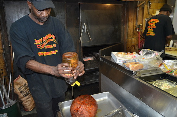 An employee at Tom's Bar-B-Q on Getwell squeezes honey onto a ham the restaurant is about to smoke.