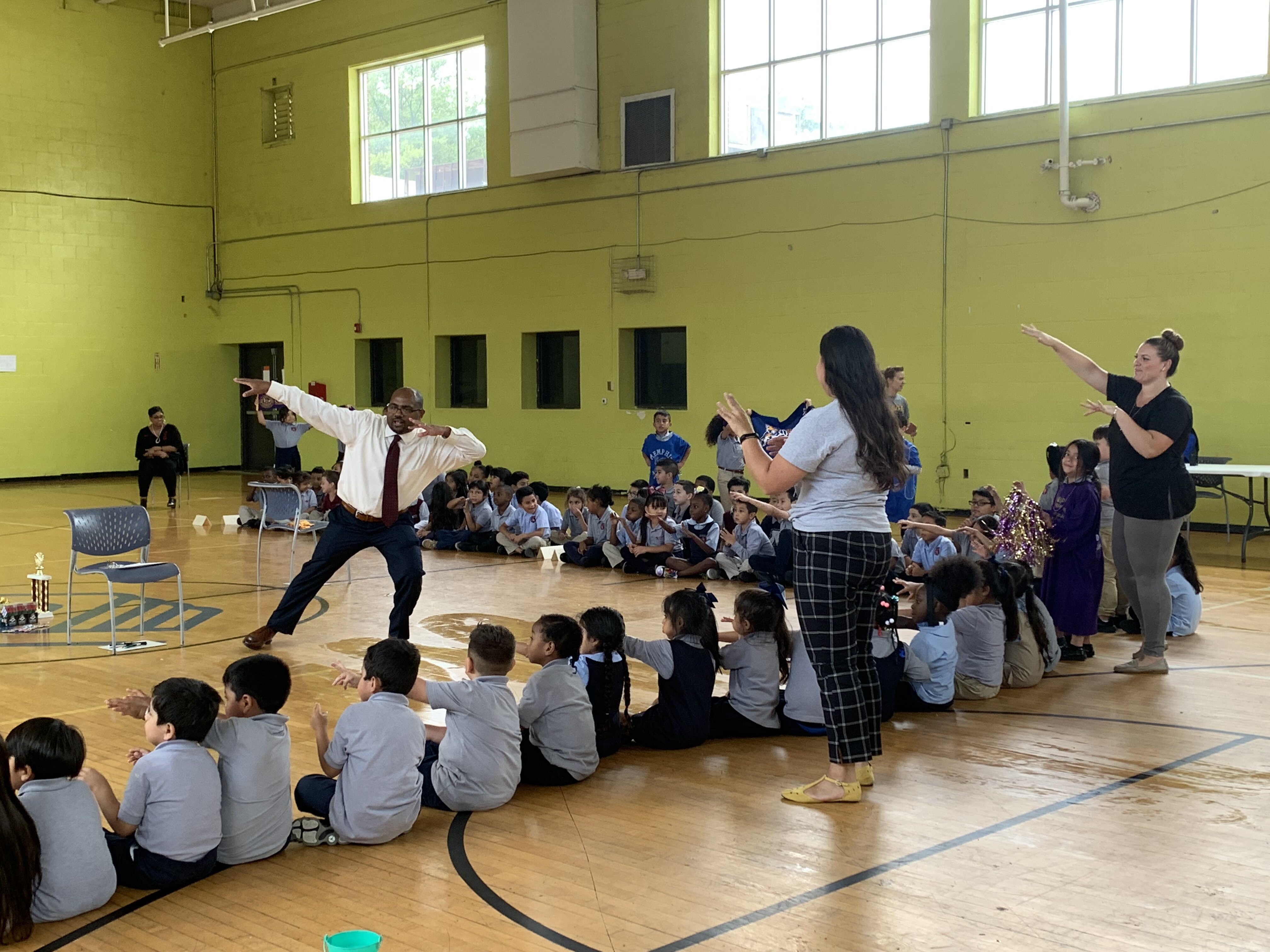 At Aurora Collegiate Academy's bi-weekly Friday Community Meeting, Dean of Students Brearn Wright leads K-2 scholars in sending "shine" or good energy to support their classmates. (Cat Evans)