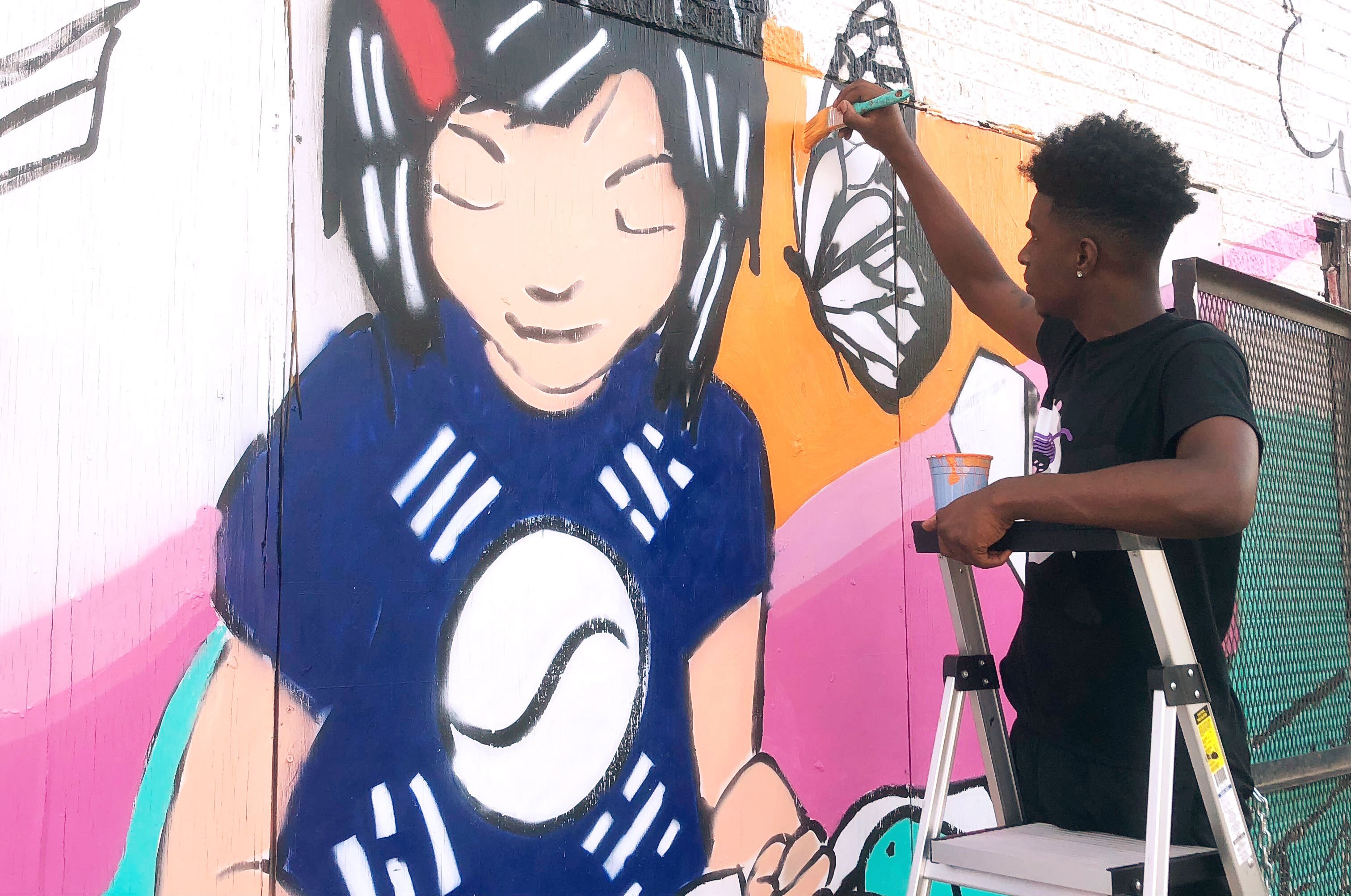 Donte Davis works on a section of the You's Grocery mural depicting store owner Ae An Sartain as a child when her father first opened the store. The artists based the mural on Sartain's memories and neighborhood history. (A.J. Dugger)