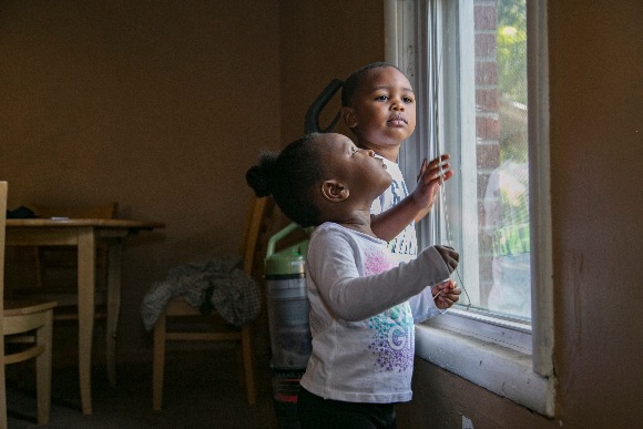 Carl, 3, and Carlee, 2, play with the blinds of the family's living room window. (Natalie Eddings)