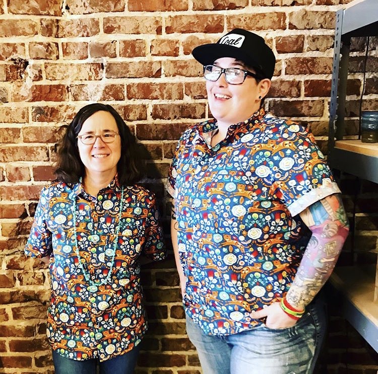 High Ground publisher and community engagement manager, Emily Trenholm (L), and managing editor, Cole Bradley (R), pose in matching shirts on an Accidental Uniform Day. (Belltower Artisans)