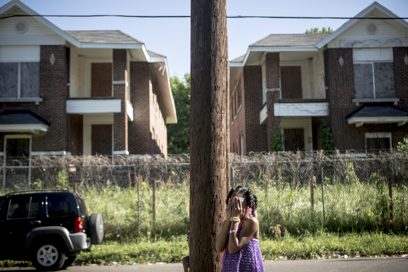 A young girl plays hide and seek in front of shuttered apartment buildings on Tate Street. (Andrea Morales)
